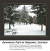 A winter scene of Downtown Park in Humenne, Slovakia, showcases tall snow-covered trees and a bench along a snowy path in this xstitch chart.