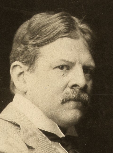 A black-and-white portrait photograph of artist Edwin Austin Abbey. He is depicted from the chest up, looking directly at the camera with a serious expression. He has short, dark hair and a neatly trimmed mustache. He is wearing a dark, formal suit jacket over a crisp white dress shirt with a tall standing collar and a dark necktie. The lighting is focused on his face against a neutral, shadowed background, capturing the dignified appearance of a successful Victorian-era academic painter.