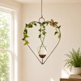 Heart-shaped copper hanging propagation vase with ivy and butterfly accent beside a sunlit window