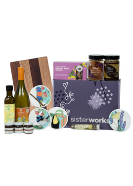 Front view of the SisterWorks Artisan Grazing Hamper contents laid out. Includes Indigiearth Lemon Myrtle Olive Oil, Munificent Wine, ShortHive Infused Honey, SisterWorks Spicy Salsa, SisterWorks Fig Jam, Kakadu Plum & Basil Crackers, Cultural Fusion Coasters, and a Nigretta of Hamilton wooden board. The purple standard gift box with SisterWorks logo is visible, showcasing a thoughtful, ethically sourced gourmet gift.
