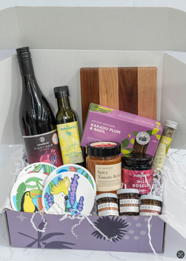 Angled view of the SisterWorks Artisan Grazing Hamper contents arranged within the purple standard gift box. Features a bottle of Munificent Wine, Indigiearth Lemon Myrtle Olive Oil, ShortHive Infused Honey, SisterWorks Spicy Salsa and Fig Jam, Kakadu Plum & Basil Crackers, Cultural Fusion Coasters, and the Nigretta of Hamilton wooden board, perfect for a thoughtful, ethically sourced gourmet gift.