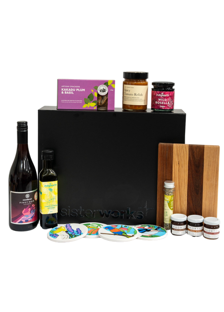 Front view of the SisterWorks Artisan Grazing Hamper contents laid out. Features Indigiearth Lemon Myrtle Olive Oil, Munificent Wine, ShortHive Infused Honey, SisterWorks Spicy Salsa, SisterWorks Fig Jam, Kakadu Plum & Basil Crackers, Cultural Fusion Coasters, and a Nigretta of Hamilton wooden board. The black premium gift box with embossed SisterWorks logo is visible in the background, signifying a luxury, ethical corporate gift