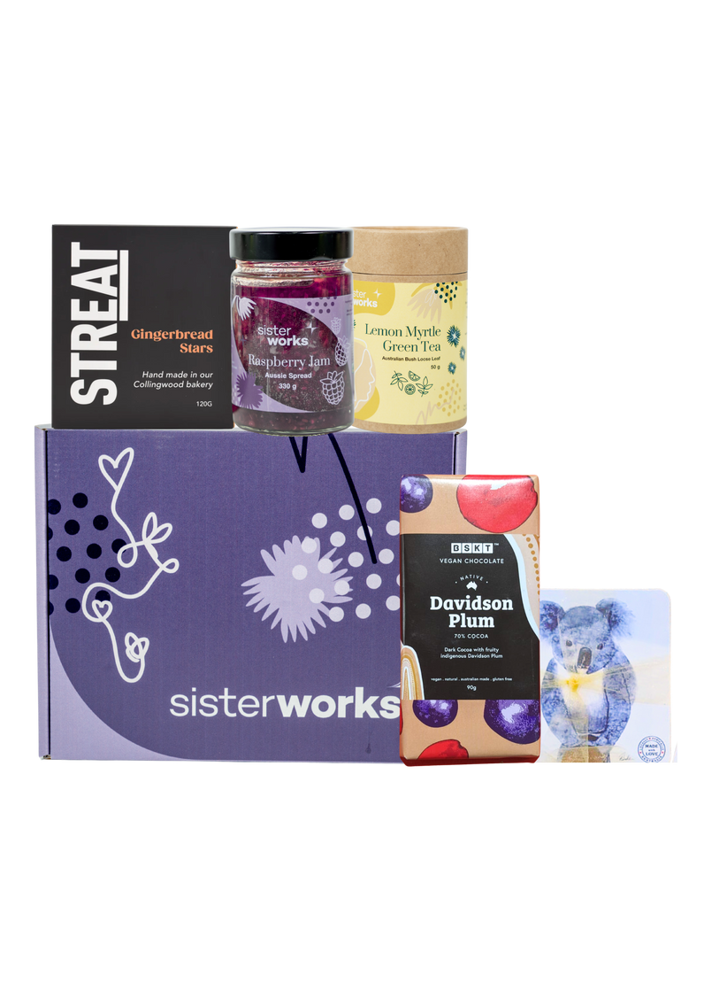 A SisterWorks Aussie Holiday Hamper. The box contains STREAT Gingerbread Stars, SisterWorks Raspberry Jam, BSKT Davidson Plum Vegan Chocolate, SisterWorks Lemon Myrtle Green Tea, and Australian Icon Coasters. The items are arranged neatly in a box, highlighting a festive and ethical gift set.