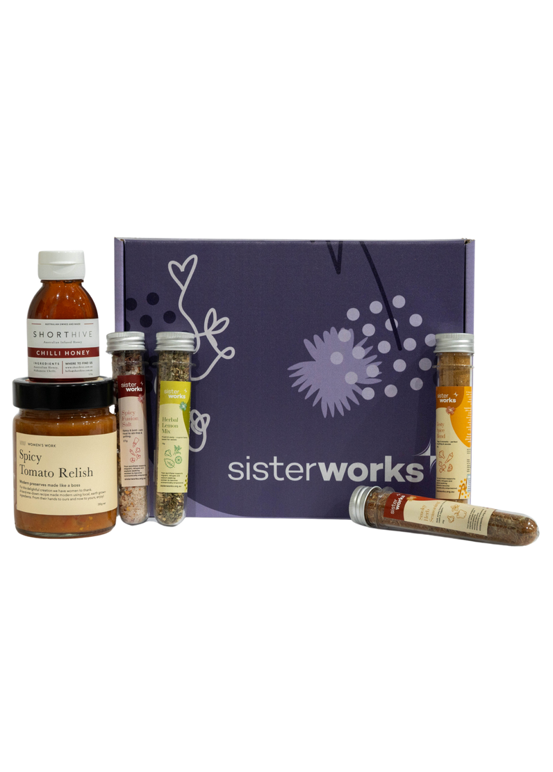An overhead view of the open SisterWorks Spice Enthusiast's Delight Hamper. The hamper contains a collection of gourmet spices, including Hot Chilli Oil, Smoky Herb Seasoning, Zesty Spice Blend, Herbal Lemon Mix, and Spicy Fusion Salt. The items are arranged in a box, highlighting a beautiful gift set for anyone who loves to cook.