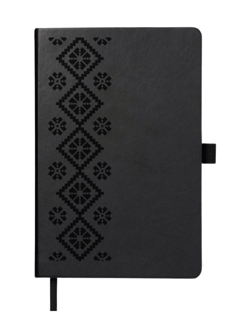 Top-down view of the black 'Embroidered Roots' Hard Cover Journal by SisterWorks against a plain green background. The full front cover is visible, featuring the detailed and embossed 'Embroidered Roots' pattern by Fernanda Rodriguez, highlighting the journal's unique artistic design.