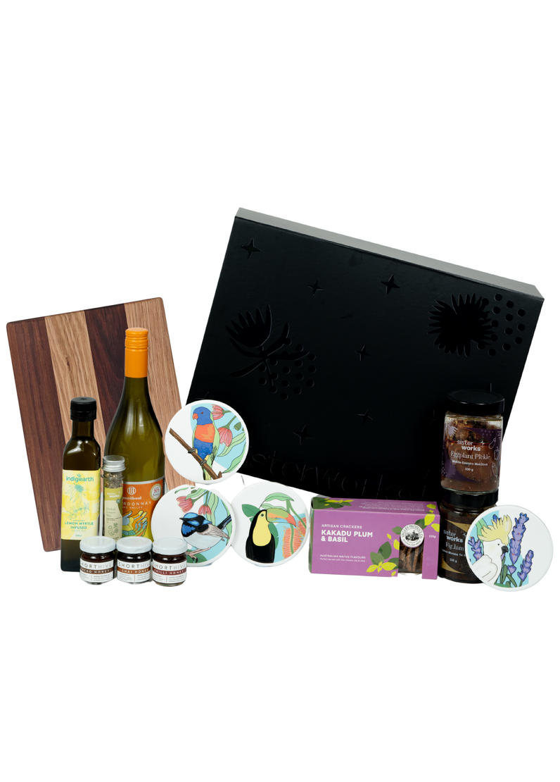 Front view of the SisterWorks Artisan Grazing Hamper contents laid out. Features Indigiearth Lemon Myrtle Olive Oil, Munificent Wine, ShortHive Infused Honey, SisterWorks Spicy Salsa, SisterWorks Fig Jam, Kakadu Plum & Basil Crackers, Cultural Fusion Coasters, and a Nigretta of Hamilton wooden board. The black premium gift box with embossed SisterWorks logo is visible in the background, signifying a luxury, ethical corporate gift