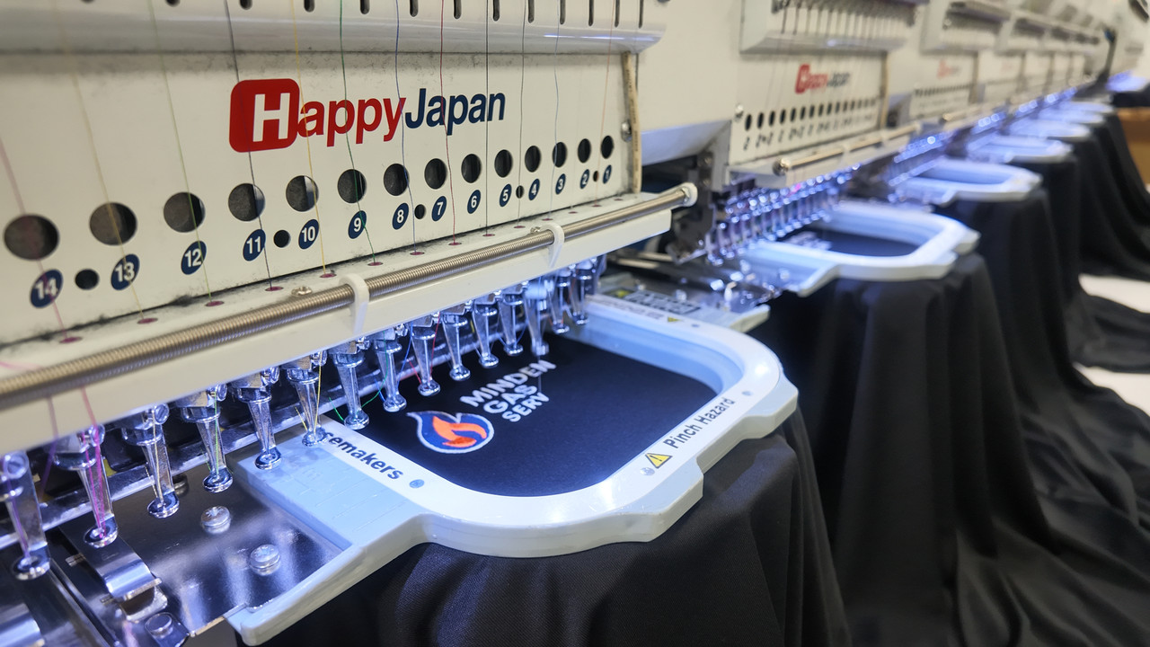 A multi-head embroidery machine mid-run, a logo being stitched in the hoop with further machine heads working down the line