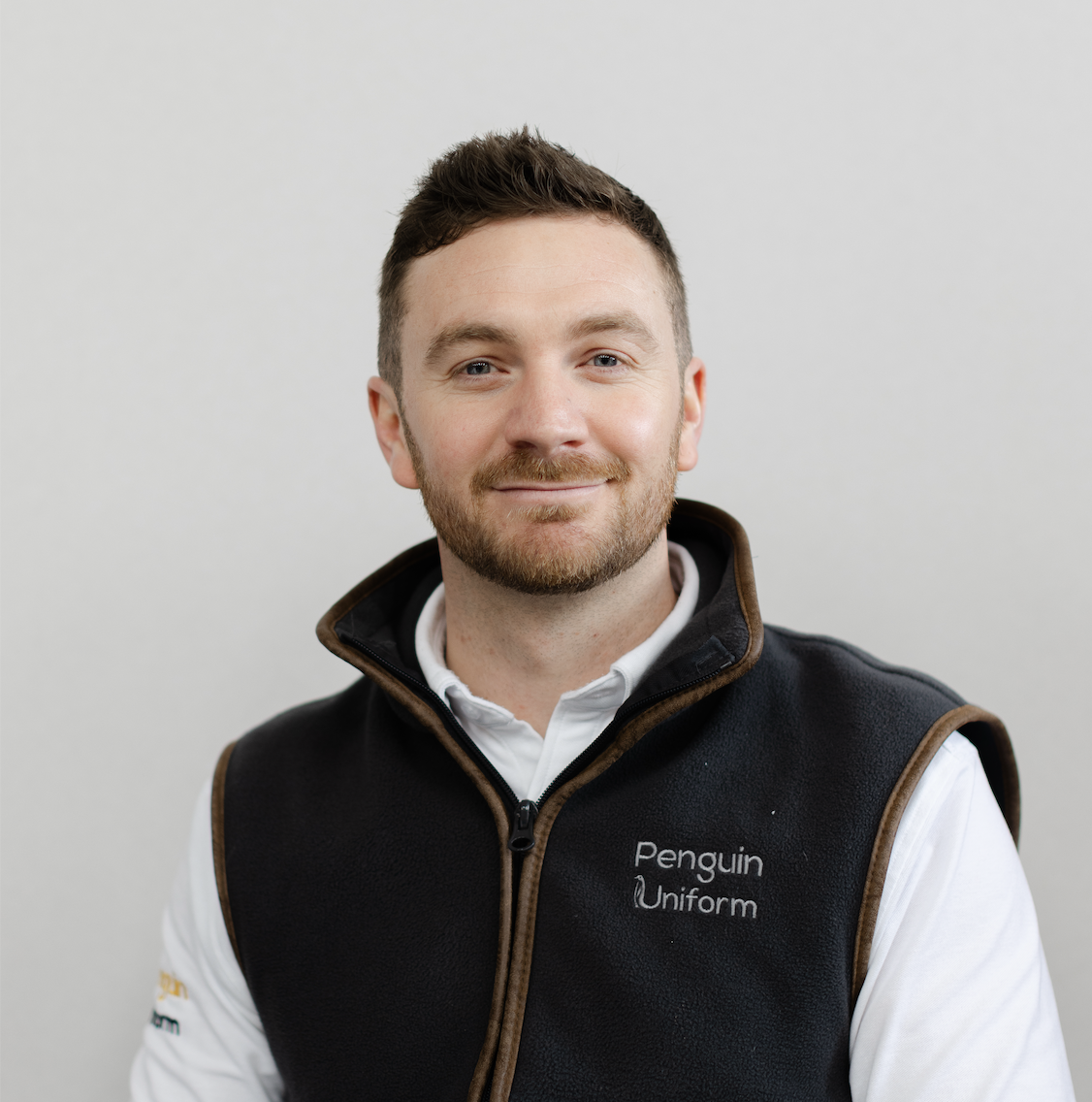 Jared, CEO and founder of Penguin Uniform, standing in the Cheltenham production facility beside embroidered garments