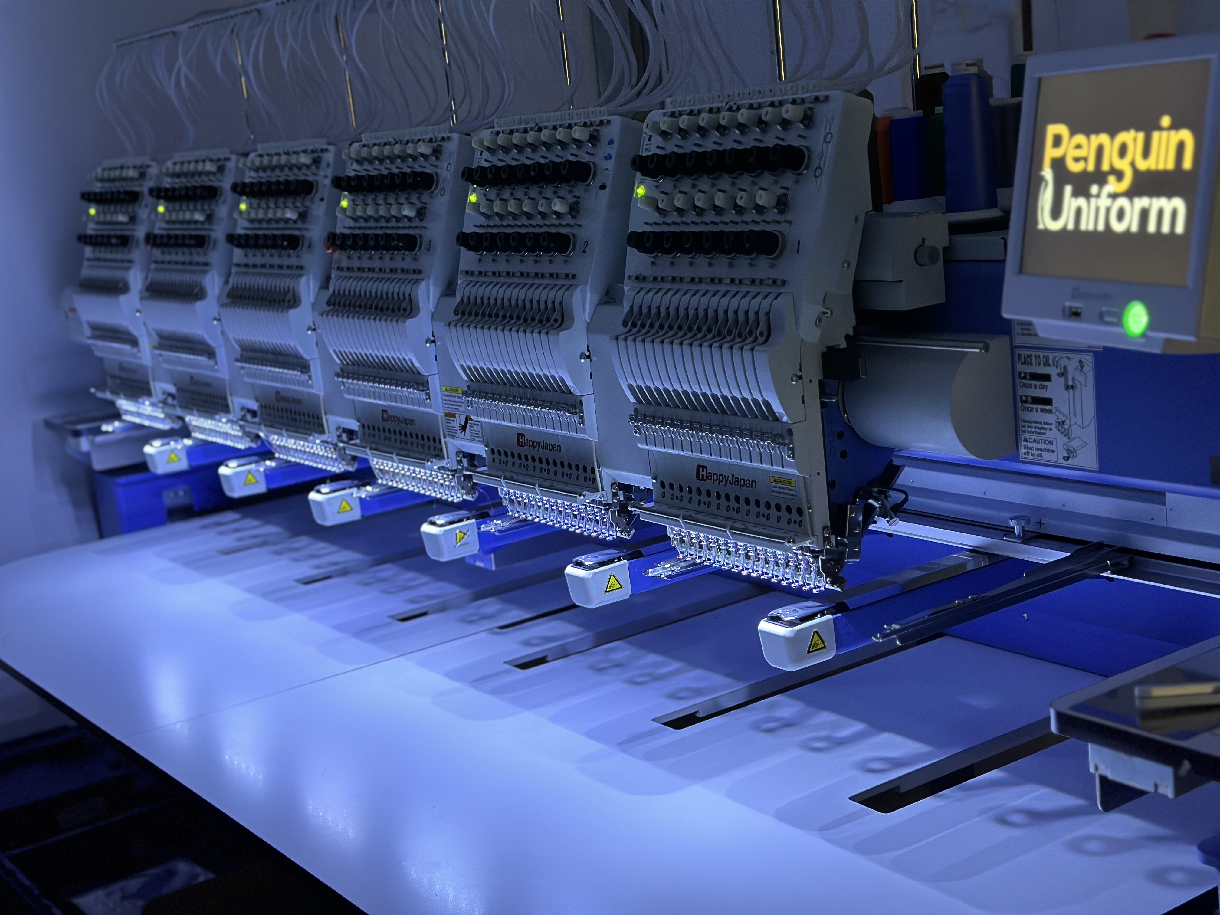 Rows of commercial embroidery heads stitching branded garments inside the Penguin Uniform Cheltenham facility