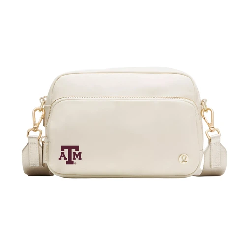Cream lululemon crossbody bag featuring a maroon Texas A&M logo on the lower front, gold lululemon emblem, front zippered pocket, gold-tone hardware, and adjustable cream shoulder strap.
