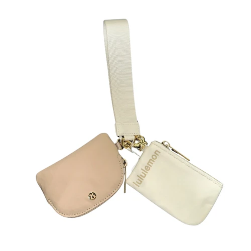 Lululemon wristlet set featuring a cream rectangular zip pouch with Lululemon lettering, beige curved zip pouch with logo accent, woven wrist strap, and gold-tone hardware.
