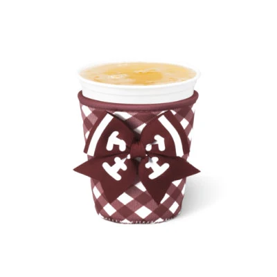 Swig Small Cup Coolie featuring a maroon and white gingham pattern, maroon trim, and dimensional football-inspired bow with white lace details, shown holding a small beverage cup.