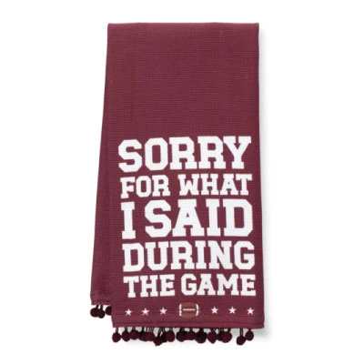 Swig maroon tea towel featuring bold white “Sorry For What I Said During The Game” lettering, star and football accents, and decorative maroon pom-pom trim along the bottom.