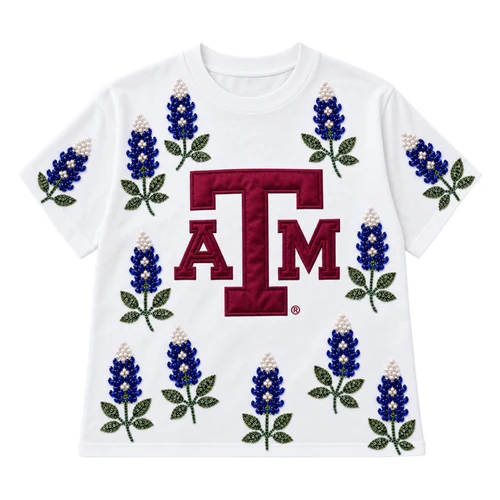 Brianna Cannon Texas A&M white shirt featuring a large maroon A&M logo surrounded by bluebonnet designs embellished with blue and white beads and green beaded leaves across the front and sleeves.