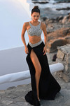 Model wearing Portia and Scarlett PS26168 black two-piece gown with silver crystal crop top and thigh-high slit skirt outdoors.