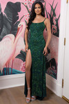 Woman wearing a Hunter Emerald fully beaded fitted gown with spaghetti straps and a high slit, posing inside.