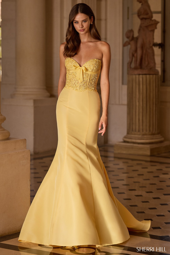Sherri Hill 57621 in Yellow with intricate lace corset bodice, dainty bow detail, and dramatic taffeta mermaid skirt.