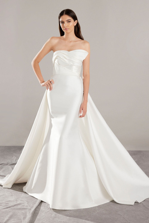This strapless mikado gown stuns with modern pleats, a structured bodice, and a detachable dramatic overskirt This strapless mikado gown stuns with modern pleats, a structured bodice, and a detachable dramatic overskirt