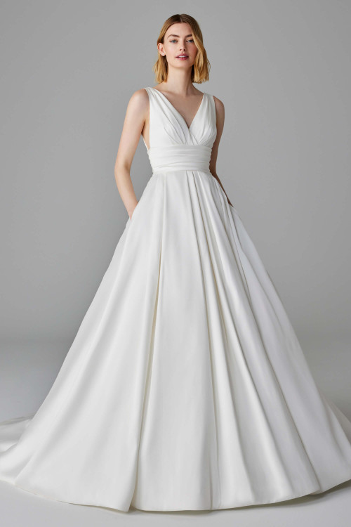 This timeless ballgown stuns with a pleated V-neck bodice, defined waist, and elegant pockets. This timeless ballgown stuns with a pleated V-neck bodice, defined waist, and elegant pockets.