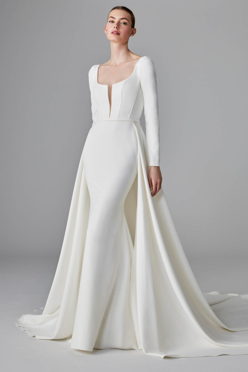 Minimalist bridal gown with long sleeves, plunging neckline, and dramatic overskirt Minimalist bridal gown with long sleeves, plunging neckline, and dramatic overskirt