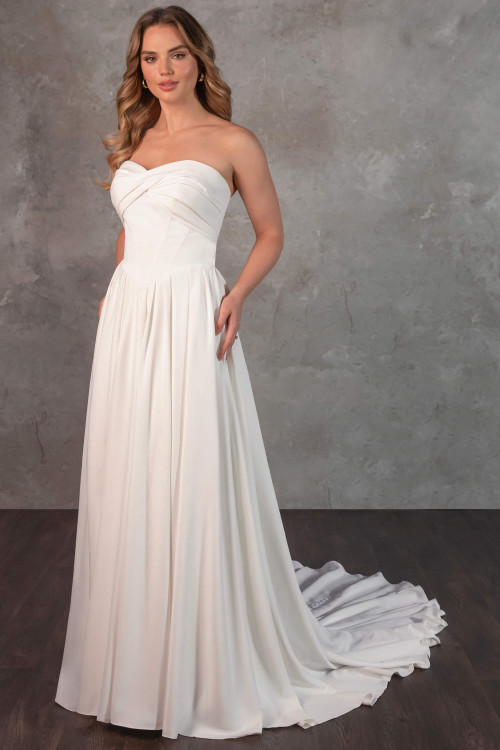 Strapless matte satin gown with modern twist bodice and flowing pleated A-line skirt. Strapless matte satin gown with modern twist bodice and flowing pleated A-line skirt.