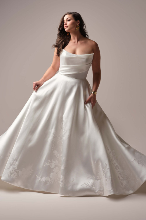 Plus-size bride wearing the Maggie Sottero Radiance A-line gown, highlighting the full satin skirt and unique folded strapless neckline. Plus-size bride wearing the Maggie Sottero Radiance A-line gown, highlighting the full satin skirt and unique folded strapless neckline.