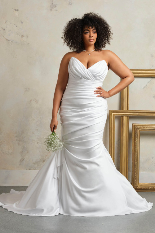 Plus-size bride wearing the Maggie Sottero Vonae trumpet gown in satin, showcasing the asymmetrical ruching Plus-size bride wearing the Maggie Sottero Vonae trumpet gown in satin, showcasing the asymmetrical ruching
