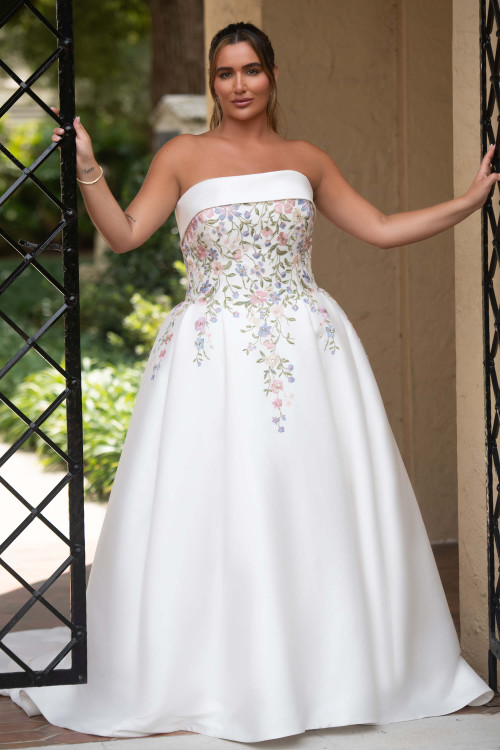 A plus size bride in the Essense of Australia D4217 ballgown, showcasing the full pleated Mikado skirt and pastel floral lace bodice. A plus size bride in the Essense of Australia D4217 ballgown, showcasing the full pleated Mikado skirt and pastel floral lace bodice.