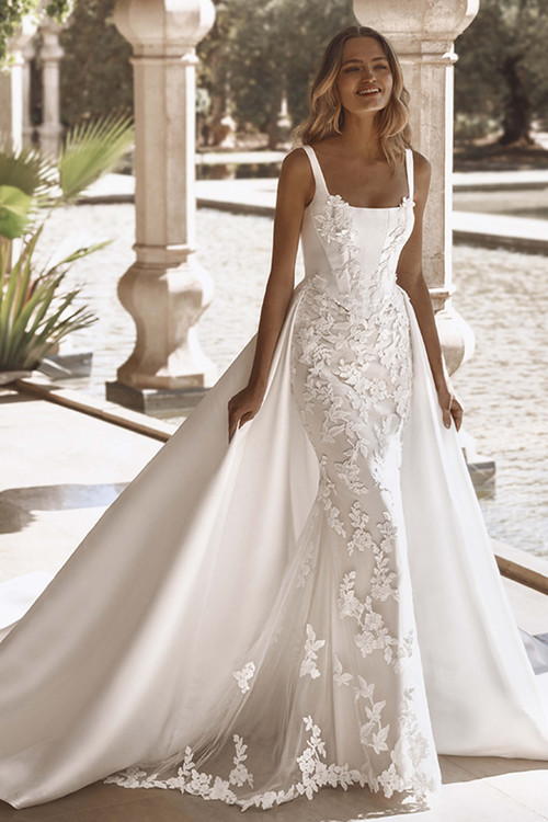 Front view of Enzoani Vee gown with square neckline, lace bodice, and flowing skirt. Front view of Enzoani Vee gown with square neckline, lace bodice, and flowing skirt.