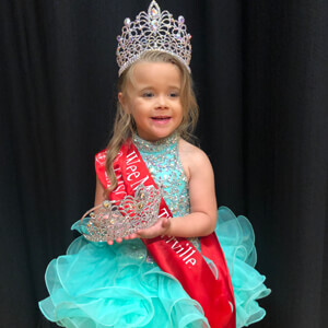 Little Miss pageant winner in white cupcake dress with tiara and sash