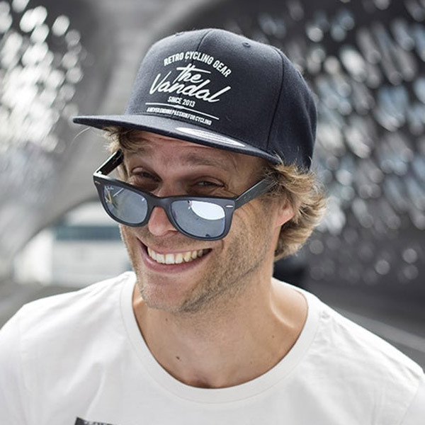 Man in cap and sunglasses smiling.