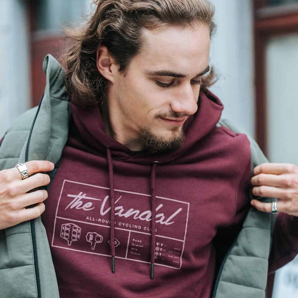Man wearing a burgundy The Vandal cycling hoodie adjusting his jacket
