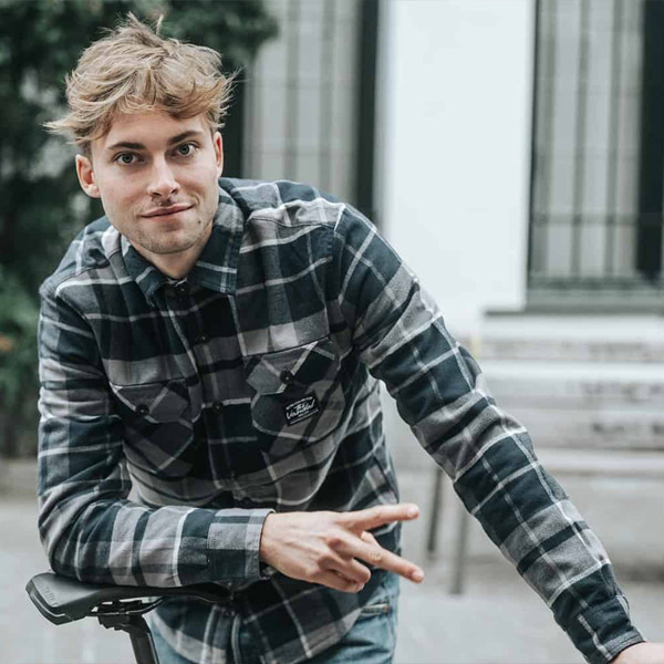 Man in casual plaid shirt posing with a peace sign while leaning on a bike