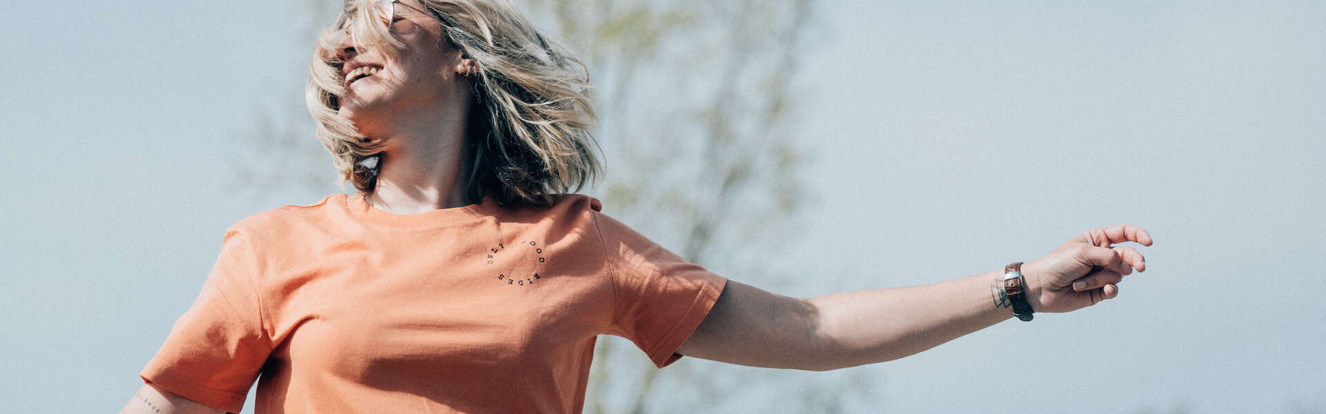 Woman smiling outdoors in an orange t-shirt under a clear sky