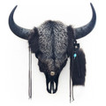 Bison skull hung on a white wall covered in dark silver fox fur with decorative leather tassels and small pieces of turquoise