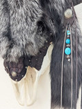 Closeup section of Bison skull wall hanging covered in silver fox fur showing detail of fur, leather tassels, and strands with turquoise and small decorative beads.
