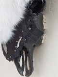 Closeup section of Bison skull wall hanging covered in white shadow fox fur showing detail of fur, dark skull bones, teeth, and dark leather accents with decorative metal rivets.