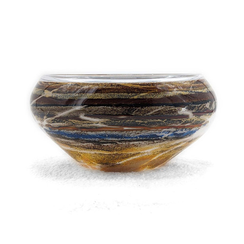 A handblown bowl-shaped glass vessel featuring layered bands of light, warm earth tones and blue accents to evoke an image of the layering found in canyon walls