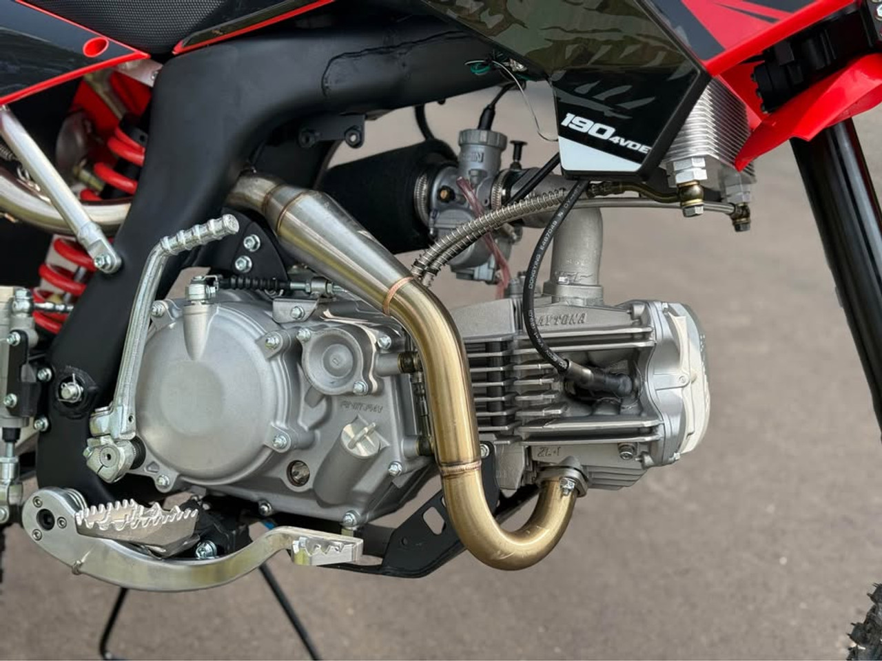 2024 Piranha Daytona 190-4V DE (Dual Exhaust), a high-performance competition pit bike designed for serious riders. The bike features a sleek and aggressive design with a dual exhaust system, emphasizing its power and performance. The Daytona Anima 190 4-valve engine and oversized oil cooler are highlighted, showcasing the bike’s robust power and efficient cooling. The ENGI adjustable suspension (800mm front forks and 330mm rear shock) is prominently displayed, underscoring the bike’s superior handling and shock absorption. The 14-inch front and 12-inch rear aluminum rims with Kenda Carlsbad tires add to the bike’s durability and traction. Overall, the image captures the essence of a high-performance, competition-ready pit bike built to dominate the track.