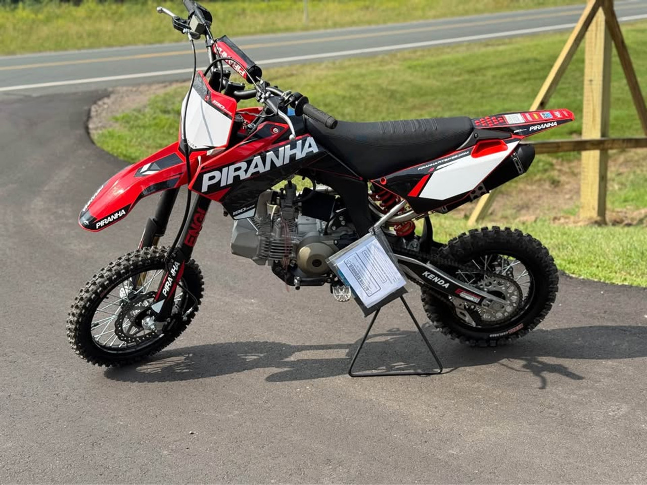 2024 Piranha Daytona 190-4V DE (Dual Exhaust), a high-performance competition pit bike designed for serious riders. The bike features a sleek and aggressive design with a dual exhaust system, emphasizing its power and performance. The Daytona Anima 190 4-valve engine and oversized oil cooler are highlighted, showcasing the bike’s robust power and efficient cooling. The ENGI adjustable suspension (800mm front forks and 330mm rear shock) is prominently displayed, underscoring the bike’s superior handling and shock absorption. The 14-inch front and 12-inch rear aluminum rims with Kenda Carlsbad tires add to the bike’s durability and traction. Overall, the image captures the essence of a high-performance, competition-ready pit bike built to dominate the track.