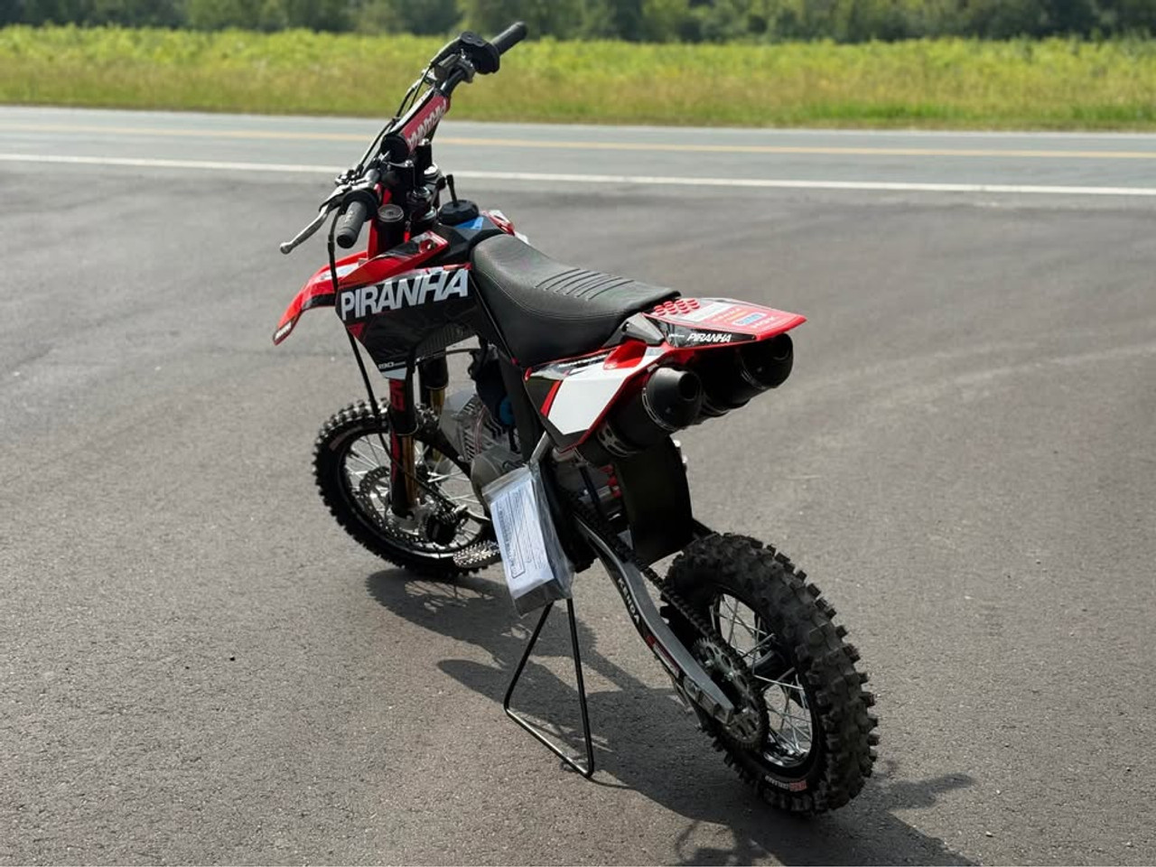 2024 Piranha Daytona 190-4V DE (Dual Exhaust), a high-performance competition pit bike designed for serious riders. The bike features a sleek and aggressive design with a dual exhaust system, emphasizing its power and performance. The Daytona Anima 190 4-valve engine and oversized oil cooler are highlighted, showcasing the bike’s robust power and efficient cooling. The ENGI adjustable suspension (800mm front forks and 330mm rear shock) is prominently displayed, underscoring the bike’s superior handling and shock absorption. The 14-inch front and 12-inch rear aluminum rims with Kenda Carlsbad tires add to the bike’s durability and traction. Overall, the image captures the essence of a high-performance, competition-ready pit bike built to dominate the track.