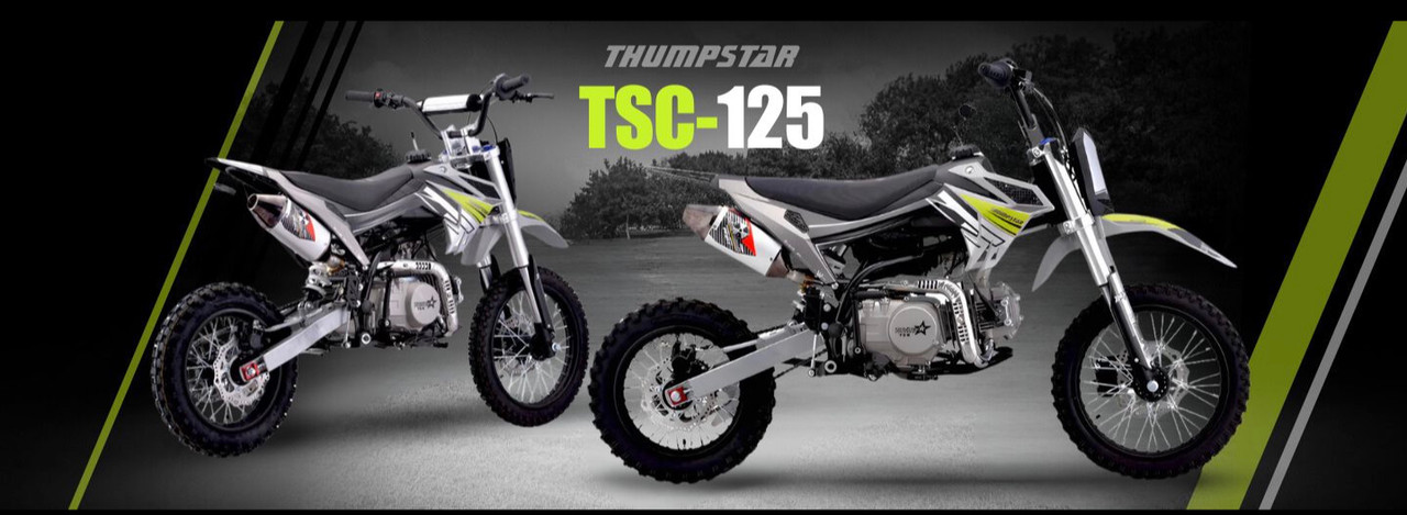 Thumpstar TSC 125 pit bike, highlighting its signature stealth plastics, wrap-around frame, and gripper striped seat. The bike is displayed in an action-ready stance, emphasizing its conventional front forks, rear mono shock, and front and rear disc brakes. The forged triple clamps and stator guard are subtly visible, underscoring the bike’s durability and safety features. The Mikuni VM22 carburetor and standard exhaust system are also highlighted, showcasing the bike’s performance enhancements.