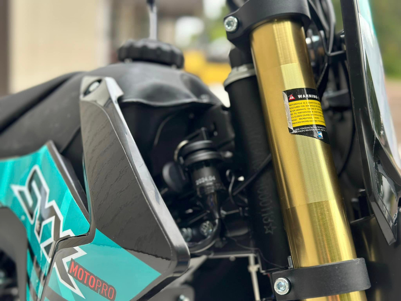 The image showcases the SYX MotoPro WHIP PAD125-3 125cc Pit Bike in one of its three available color options. The bike features a sleek design with upgraded graphics and plastics, highlighting its modern and aggressive look. The anodized hydraulic front fork and coil spring rear shock absorber are visible, emphasizing the bike's advanced suspension system. The heavy-duty black steel rims with off-road tires and hydraulic disc brakes are prominently displayed, showcasing the bike's durability and safety features. The handlebar with a built-in hour meter and the SY-Forged triple clamp add to the bike's premium feel. Overall, the image captures the essence of a high-performance, stylish, and durable pit bike ready for any off-road adventure.