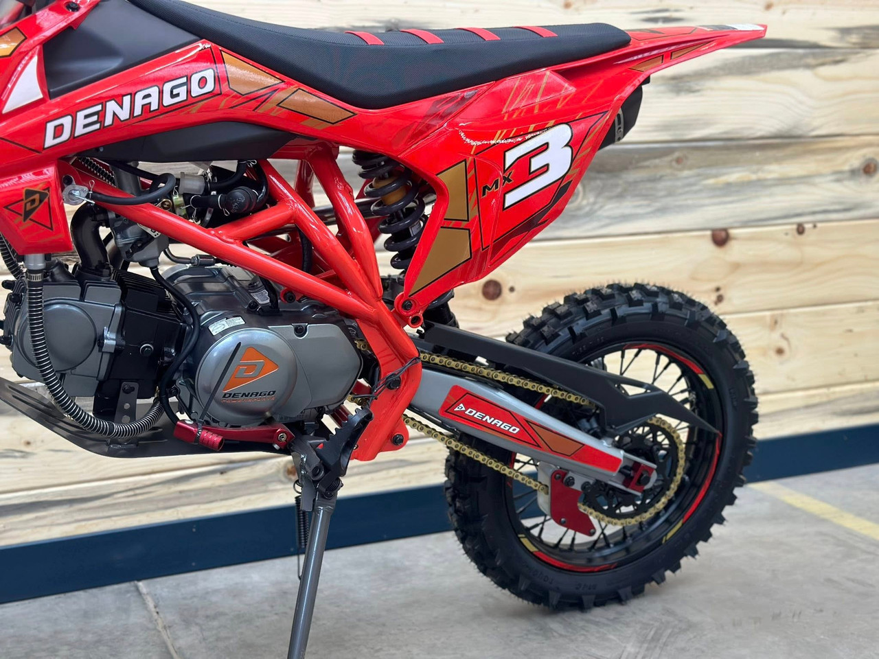 Denago MX3 Red Edition 140cc Pit Bike with bold red graphics, black powder-coated wheels, stainless steel exhaust, gold drive chain, and CNC anodized components for trail and off-road riding.