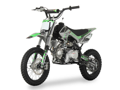 Syx Moto PAD125-1S 125cc semi-automatic pit bike featuring a black steel frame, aggressive new plastics design, and knobby off-road tires. The bike is shown in an off-road setting, highlighting its front hydraulic disc brake, remote oil cooler, and dual start system. The 14-inch front wheel and 12-inch rear wheel with heavy-duty spokes are clearly visible.