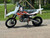 2025 Kayo TD 125TD 125, a sleek and modern dirt bike designed for off-road enthusiasts. The bike features a bold design with a black and red color scheme, highlighting its aggressive yet stylish appearance. The inverted front forks and single rear shock suspension are prominently visible, emphasizing the bike's superior handling and stability. The knobby tires (60/100-14 front and 80/100-12 rear) are shown gripping the terrain, showcasing their traction and durability. The 123.7 cc SOHC 4-stroke engine is centrally located, with the air-cooled system visible for efficient heat dissipation. The front and rear disc brakes are clearly displayed, highlighting the bike's safety features. The 29.5-inch seat height and 165 lbs lightweight frame make it accessible for riders of all skill levels. The image captures the bike in an off-road setting, ready to tackle dirt trails, rocky paths, and challenging terrains.