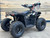 The image features the Denago E-Hawk 6 ATV, a sleek and modern electric ATV designed for kids aged 6 and up. The ATV showcases a bold black finish with multicolored LED lights, giving it a stylish and futuristic look. The rugged all-terrain tires (AT 16 x 8-7) and double A-arm front suspension highlight its capability to handle various terrains, from dirt trails to grassy fields. The handlebar-mounted controls, including the push-button gear selector and keyed ignition, are clearly visible, emphasizing the ATV's user-friendly design. The compact dimensions (51" x 31" x 32.5") and low seat height (23.5") make it perfectly sized for young riders, while the 48V removable lithium-ion battery and 1600W brushless electric motor underscore its eco-friendly and high-performance features. Safety elements like dual hydraulic disk brakes and an anti-theft alarm are subtly integrated into the design. This image captures the essence of the E-Hawk 6 ATV as a safe, fun, and technologically advanced electric vehicle for kids.