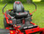 Toro 50" TimeCutter Max MyRide Zero Turn Mower (77502), highlighting its innovative MyRIDE® Suspension System with a close-up of the large spring coil. This feature isolates the operator from rough terrain, providing a smooth and comfortable ride while mowing. The mower’s heavy-duty steel IronForged® Deck is prominently displayed, emphasizing its durability and ability to handle tough mowing conditions. The beefy hybrid-tread rear tires are shown for maximum traction, ensuring the mower can navigate any terrain without damaging the turf. Additionally, the image highlights the spray-blocking fenders, which prevent debris and water from splashing onto the engine or operator. The automotive-style fuel fill and integrated drain hose are also visible, showcasing the mower’s user-friendly maintenance features. With its ultra-strong, fully tubular steel frame and 23 hp Kawasaki engine, this zero-turn mower is designed for professional-grade performance and residential comfort.