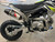 Thumpstar TSK 90cc mini bike, featuring its sleek mini stealth plastics, compact frame, and bold design. The bike is displayed in an action-ready stance, highlighting its inverted front suspension, oversized disc brakes, and Pipe Bomb muffler. The wrap-around frame and waterproof wiring are subtly visible, emphasizing the bike’s durability. The image also highlights the adjustable throttle limiter and emergency lanyard kill switch, key safety features for junior riders. Thumpstar TSK 90cc mini bike, featuring its sleek mini stealth plastics, compact frame, and bold design. The bike is displayed in an action-ready stance, highlighting its inverted front suspension, oversized disc brakes, and Pipe Bomb muffler. The wrap-around frame and waterproof wiring are subtly visible, emphasizing the bike’s durability. The image also highlights the adjustable throttle limiter and emergency lanyard kill switch, key safety features for junior riders.
