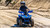 The image features the Denago E-Hawk 6 ATV, a sleek and modern electric ATV designed for kids aged 6 and up. The ATV showcases a bold black finish with multicolored LED lights, giving it a stylish and futuristic look. The rugged all-terrain tires (AT 16 x 8-7) and double A-arm front suspension highlight its capability to handle various terrains, from dirt trails to grassy fields. The handlebar-mounted controls, including the push-button gear selector and keyed ignition, are clearly visible, emphasizing the ATV's user-friendly design. The compact dimensions (51" x 31" x 32.5") and low seat height (23.5") make it perfectly sized for young riders, while the 48V removable lithium-ion battery and 1600W brushless electric motor underscore its eco-friendly and high-performance features. Safety elements like dual hydraulic disk brakes and an anti-theft alarm are subtly integrated into the design. This image captures the essence of the E-Hawk 6 ATV as a safe, fun, and technologically advanced electric vehicle for kids.
